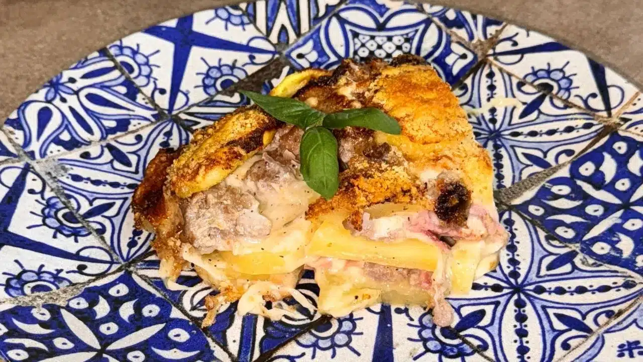 Come preparare la parmigiana di patate ricca con salsiccia, prosciutto e scamorza.