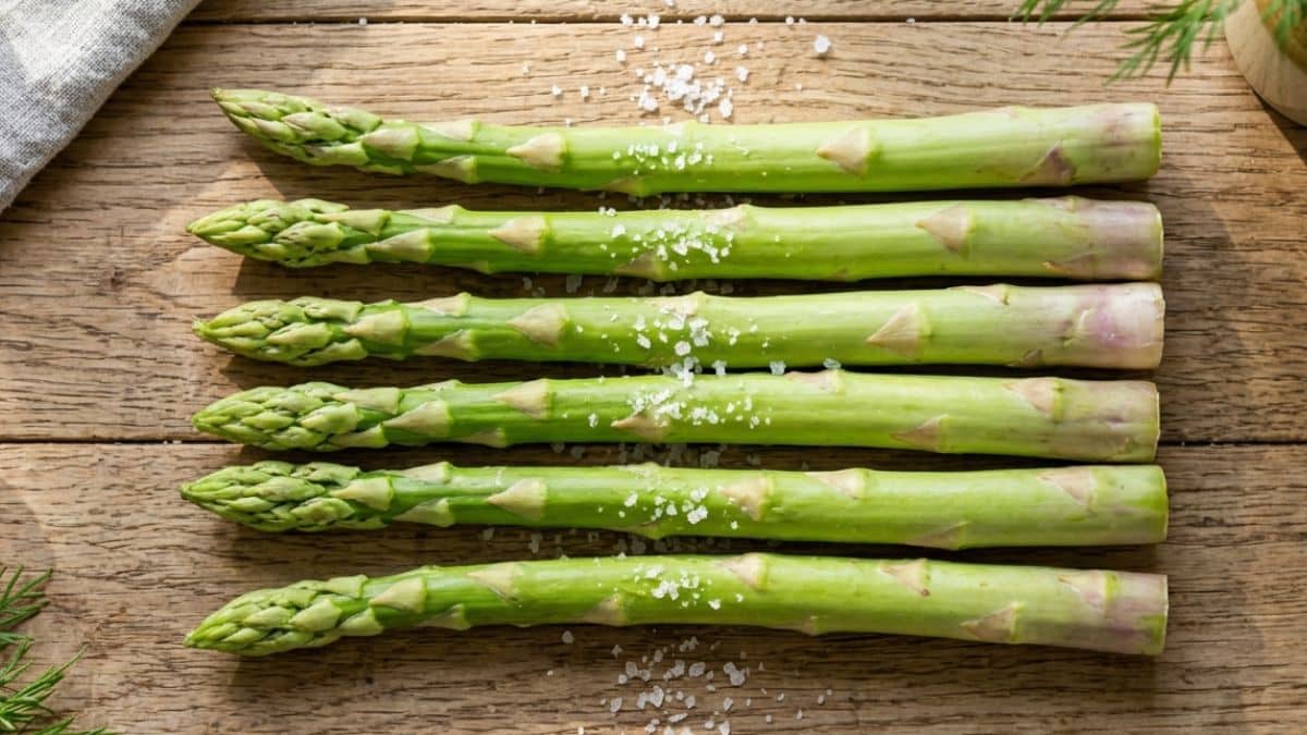 Asparagi verdi freschi conditi con sale e limone su un piano di legno.