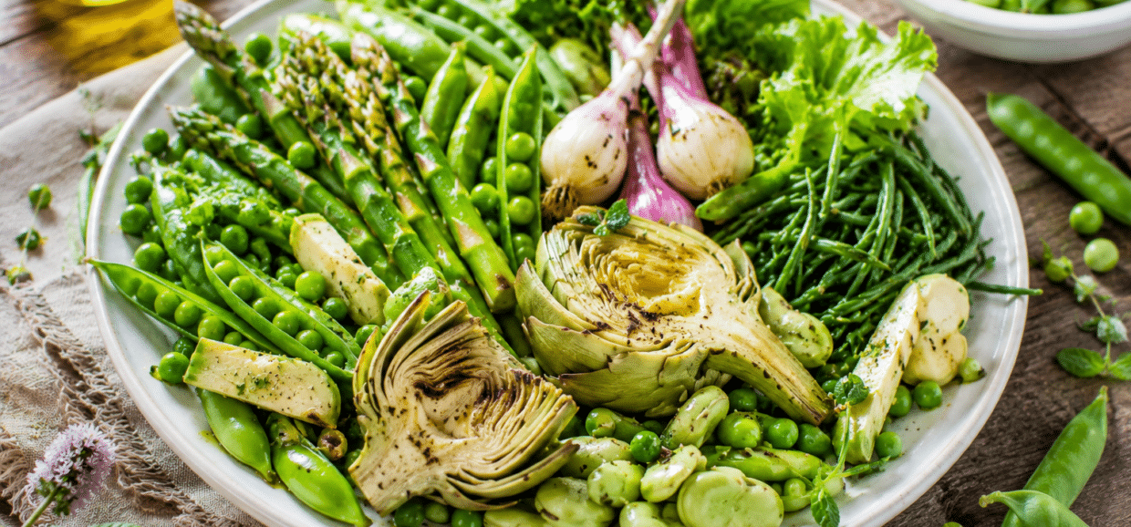 Composizione di verdure di primavera fresche con carciofi, asparagi e fave su un tavolo.